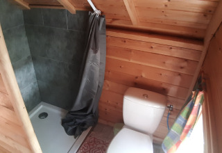 Petite salle de bain en bois dans une Finnish kota avec douche, toilettes et fenêtre au camping Ushuaïa Villages Le Viaduc.