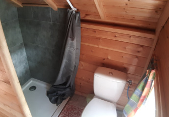 Petite salle de bain en bois dans une Finnish kota avec douche, toilettes et fenêtre au camping Ushuaïa Villages Le Viaduc.