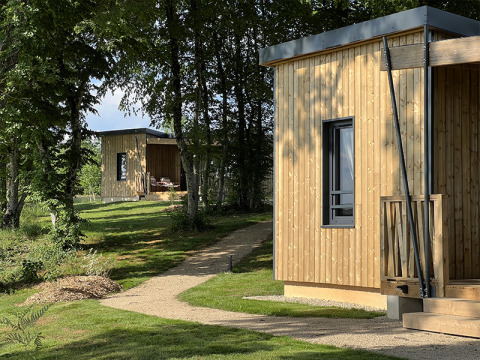 Two wooden cabins at Lodge at Campsite La Nouvelle Croze in France, surrounded by green trees and lawn