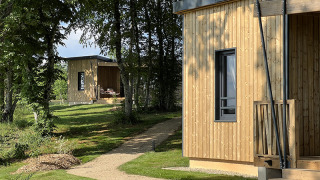 Two wooden cabins at Lodge at Campsite La Nouvelle Croze in France, surrounded by green trees and lawn