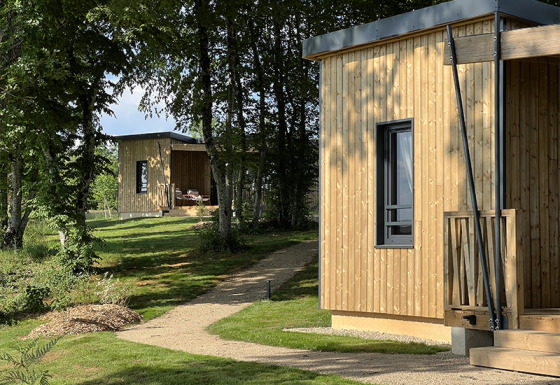Two wooden cabins at Lodge at Campsite La Nouvelle Croze in France, surrounded by green trees and lawn