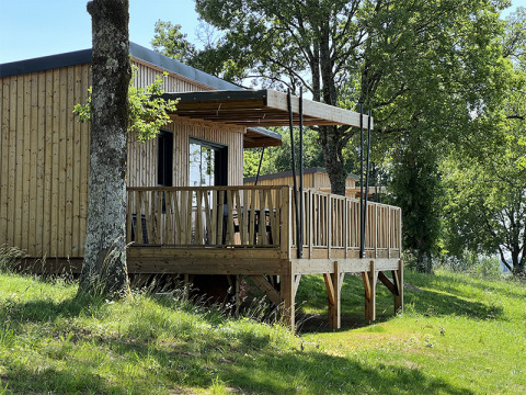 Lodge en bois sur pilotis au camping La Nouvelle Croze en France, entouré d’arbres et d’herbe verte.