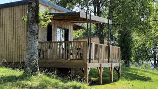 Trælodge på pæle på La Nouvelle Croze campingplads i Frankrig, omgivet af grønne træer og græs.