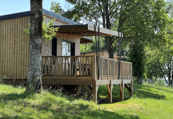Wooden lodge on stilts at Campsite La Nouvelle Croze in France, surrounded by lush trees and grass.