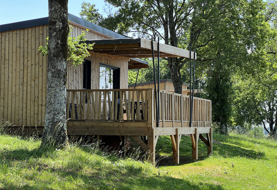 Lodge en bois sur pilotis au camping La Nouvelle Croze en France, entouré d’arbres et d’herbe verte.