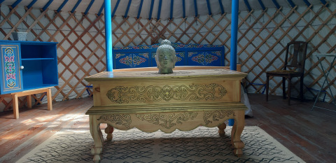 Interieur van een traditionele yurt met houten tafel, Boeddhabeeld en kleurrijk meubilair in Frankrijk.