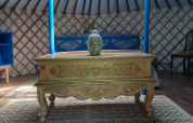 Intérieur d’une yourte traditionnelle avec une table sculptée, tête de Bouddha et meubles colorés en France.