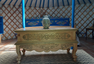 Interieur van een traditionele yurt met houten tafel, Boeddhabeeld en kleurrijk meubilair in Frankrijk.