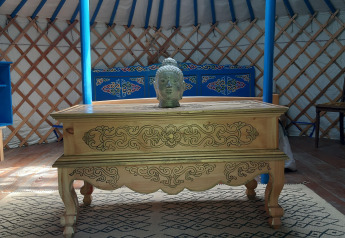 Innenraum einer traditionellen Jurte mit geschnitztem Tisch, Buddha-Kopf und bunten Möbeln in Frankreich.