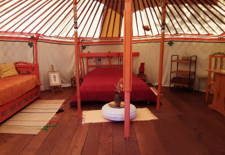 Intérieur d'une yourte traditionnelle avec mobilier en bois et lit au camping Ushuaïa Villages Le Viaduc.