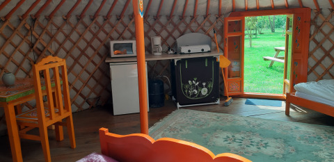 Binnenkant van een yurt met felgekleurde meubels, keukenhoek en zicht op het groene gras buiten.