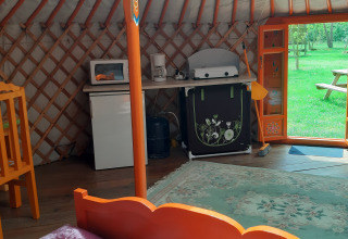 Interno di una yurta con mobili colorati, angolo cottura e porta aperta su un prato verde esterno.