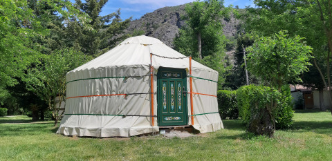 Yourte traditionnelle avec porte décorée au camping Ushuaïa Villages Le Viaduc en France, entourée de verdure.