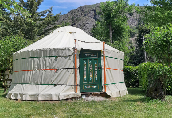 Traditionele yurt met versierde deur op Campsite Ushuaïa Villages Le Viaduc in Frankrijk, omringd door groen.