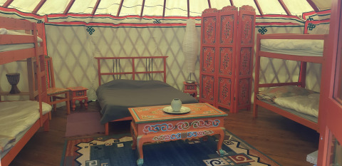 Interior of a traditional yurt with painted furniture, a double bed and bunks at Ushuaïa Villages Le Viaduc.