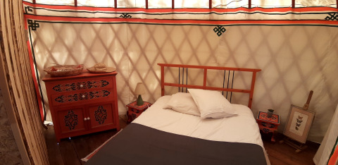 Camera accogliente con letto e mobili tradizionali in una yurta presso Ushuaïa Villages Le Viaduc in Francia.