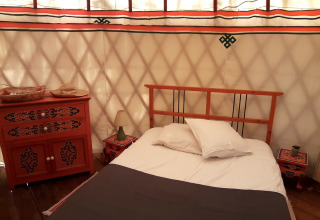 Camera accogliente con letto e mobili tradizionali in una yurta presso Ushuaïa Villages Le Viaduc in Francia.