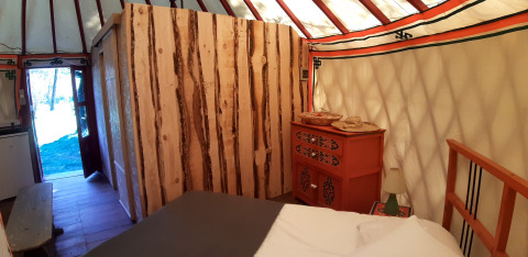 Interno di una yurta accogliente con pareti in legno, letto e comò al campeggio Ushuaïa Villages Le Viaduc, Francia.