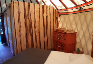 Interno di una yurta accogliente con pareti in legno, letto e comò al campeggio Ushuaïa Villages Le Viaduc, Francia.