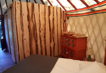 Innenansicht einer gemütlichen Jurte mit Holzwänden, Bett und Kommode im Ushuaïa Villages Le Viaduc, Frankreich.
