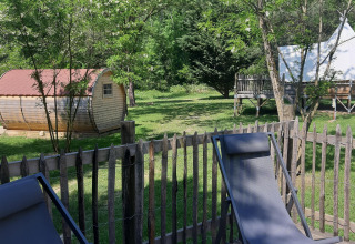 Area esterna rilassante con recinto in legno, sedie a sdraio, baita e tenda tipì al Tipi Lodge in Francia.