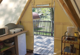 Vista interna della Tipi Lodge al Campeggio Ushuaïa Villages Le Viaduc con angolo cucina e terrazza in legno.