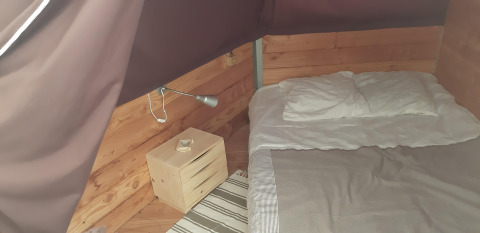 Vista interna del Tipi Lodge al Campeggio Ushuaïa Villages Le Viaduc con letto e comodino in legno.
