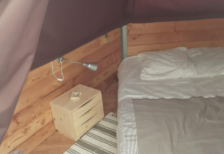 Vista interna del Tipi Lodge al Campeggio Ushuaïa Villages Le Viaduc con letto e comodino in legno.