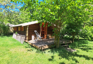 Sunny view of a log cabin with a deck and chair surrounded by trees at Campsite Ushuaïa Villages Le Viaduc.