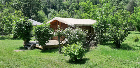 Træhytte med overdækket terrasse omgivet af grønt på Campsite Ushuaïa Villages Le Viaduc i Frankrig.