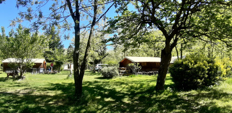 Chalets en bois au camping Ushuaïa Villages Le Viaduc en France, entourés d’arbres et de pelouse verdoyante.
