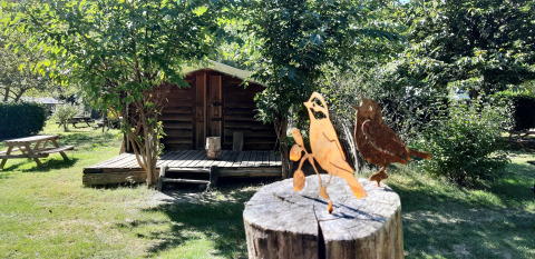 Figurines d'oiseaux en bois sur un poteau devant un chalet au camping Ushuaïa Villages Le Viaduc en France.