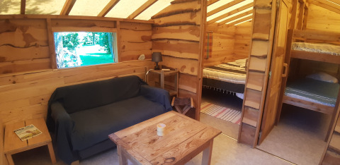 Cozy log cabin interior with sofa, table, lamp, double bed and bunk beds at Campsite Ushuaïa Villages Le Viaduc.