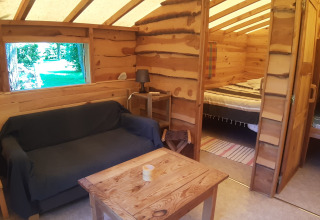 Cozy log cabin interior with sofa, table, lamp, double bed and bunk beds at Campsite Ushuaïa Villages Le Viaduc.