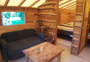 Intérieur de cabane en bois avec canapé, table, lampe, lit double et lits superposés à Ushuaïa Villages Le Viaduc.