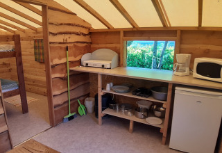Interior of a log cabin at Campsite Ushuaïa Villages Le Viaduc, featuring kitchen appliances and bunk beds.