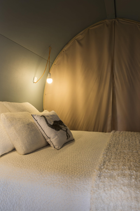Cozy bed and lighting inside the Coco Sweet safari tent at Ushuaïa Villages Le Viaduc campsite in France.