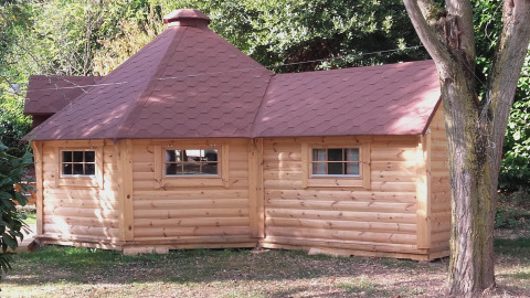 Finnische Kota-Hütte mit rotem Dach auf dem Campingplatz Ushuaïa Villages Le Viaduc, umgeben von Bäumen.