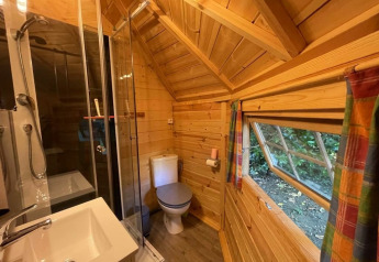 Salle de bain en bois d'une kota finlandaise au camping Ushuaïa Villages Le Viaduc, avec douche et fenêtre.