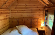 Cozy wooden Finnish kota lodge bedroom with bed, lamp, window, and towels at Campsite Ushuaïa Villages Le Viaduc, France.