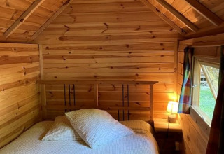 Cozy wooden Finnish kota lodge bedroom with bed, lamp, window, and towels at Campsite Ushuaïa Villages Le Viaduc, France.