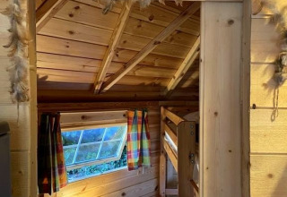 Intérieur d’un chalet en bois avec lits superposés, lampe et rideaux au camping Ushuaïa Villages Le Viaduc.