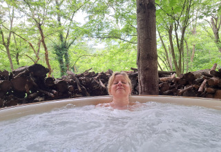 Femme se détend dans un jacuzzi extérieur dans la cabane dans les arbres au camping Ushuaïa Villages Le Viaduc, France.