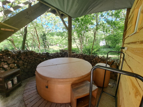 Runder Whirlpool mit Abdeckung unter Überdachung, von Bäumen und Brennholz nahe einem Baumhaus umgeben.