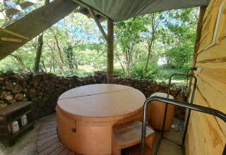Runder Whirlpool mit Abdeckung unter Überdachung, von Bäumen und Brennholz nahe einem Baumhaus umgeben.