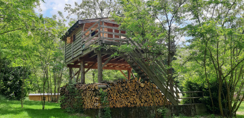 Cabane en bois sur pilotis entourée d’arbres verts avec des bûches en dessous, au camping Ushuaïa Villages Le Viaduc.