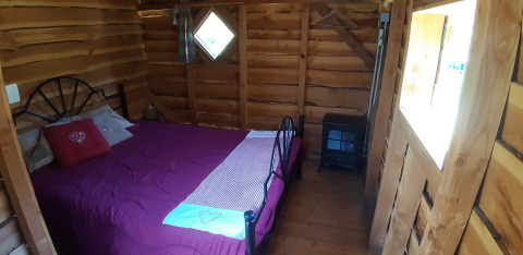 Dormitorio en casa del árbol con paredes de madera, ropa de cama morada y estufa en Le Viaduc, Francia.