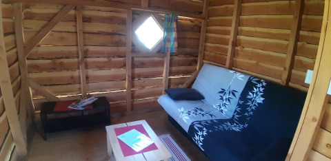 Innenraum eines Baumhauses auf dem Campingplatz Ushuaïa Villages Le Viaduc in Frankreich mit Sofa.
