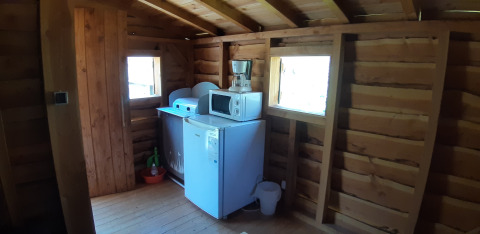 Coin d'une cabane dans les arbres au Camping Ushuaïa Villages Le Viaduc, France, avec frigo et micro-ondes.