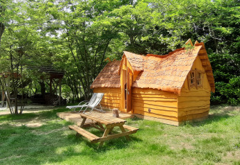 Lille træhus kaldet Magic hut på Campsite Ushuaïa Villages Le Viaduc i Frankrig, omgivet af grønne træer.